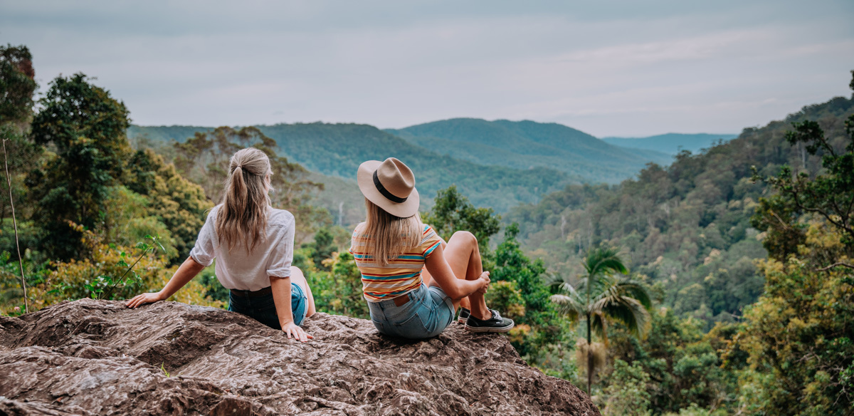 two people sitting on top of a mountainside looking at the hinterland view