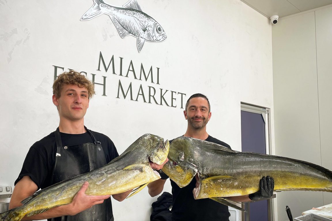 Two men holding up fish in a fish market